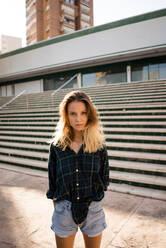 Schöne junge Frau in Shorts und Shirt steht in der Nähe von Schritten und Gebäude auf der Straße Stadt - ADSF06589