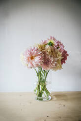 Holztisch mit Geschirr und Blumenstrauß mit frischen Blüten in einer Vase mit Wasser in der Nähe der weißen Wand - ADSF06738