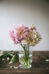 Holztisch mit Geschirr und Blumenstrauß mit frischen Blüten in einer Vase mit Wasser in der Nähe der weißen Wand - ADSF06739