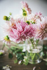 Holztisch mit Geschirr und Blumenstrauß mit frischen Blüten in einer Vase mit Wasser in der Nähe der weißen Wand - ADSF06740