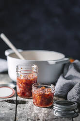 Mit roter Orangenmarmelade gefüllte Gläser auf einem rustikalen Holztisch. - ADSF06751