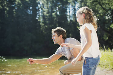 Father and daughter skipping stones at lakeside - CAIF29129