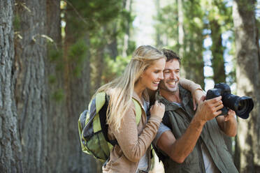 Couple looking at digital camera in woods - CAIF29130