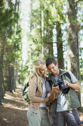 Smiling couple looking at digital camera in woods - CAIF29132