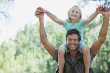 Smiling father carrying daughter on shoulders in woods - CAIF29133