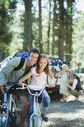 Smiling father and daughter on bicycles in woods - CAIF29139