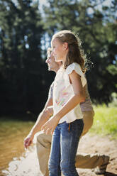 Smiling father and daughter skipping stones at lakeside - CAIF29140