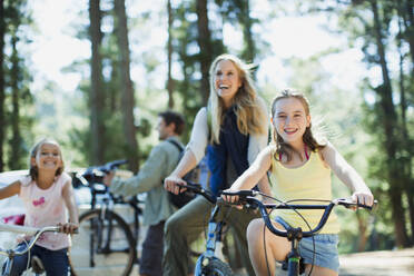 Smiling family bike riding in woods - CAIF29141