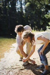 Vater und Tochter sammeln Steine am Strand am Seeufer - CAIF29145