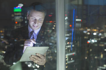 Businessman using digital tablet in urban window at night - CAIF29215