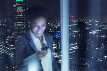 Smiling businesswoman checking cell phone in urban window - CAIF29219