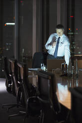 Businessman working at laptop in conference room at night - CAIF29226