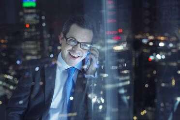 Geschäftsmann, der nachts in einem städtischen Fenster mit seinem Handy telefoniert - CAIF29258