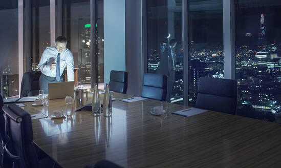 Businessman working late at laptop in conference room - CAIF29264