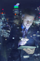 Businessman using digital tablet in urban window at night - CAIF29283