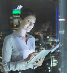 Businesswoman using digital tablet in urban window at night - CAIF29300