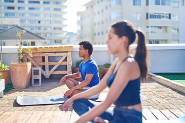 Junger Mann und Frau üben Yoga auf einem sonnigen städtischen Dach - CAIF29333