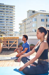 Junger Mann und Frau üben Yoga auf einem sonnigen städtischen Dach - CAIF29334