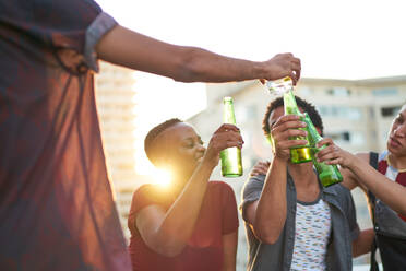 Junge Freunde stoßen mit Biergläsern auf einem sonnigen Hausdach an - CAIF29336