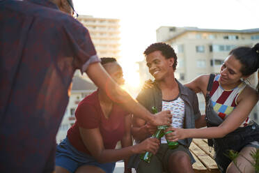 Happy young friends drinking beer on sunny urban rooftop balcony - CAIF29354