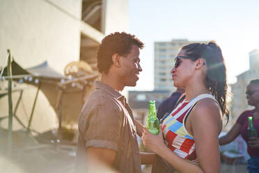 Glückliches junges Paar trinkt Bier und unterhält sich auf einem sonnigen städtischen Dach - CAIF29357