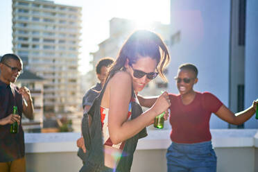 Glückliche junge Freunde tanzen und trinken Bier auf einem sonnigen städtischen Dach - CAIF29365