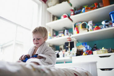 Boy sitting in bed in his room playing with toy - CAIF29461