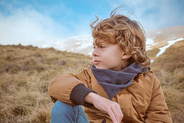 Cute boy sitting on hill near brook - ADSF06991