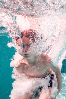 Ein Junge in Badehose taucht in das transparente blaue Wasser eines Schwimmbeckens. - ADSF07004