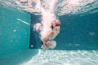 Ein Junge in Badehose taucht in das transparente blaue Wasser eines Schwimmbeckens. - ADSF07005