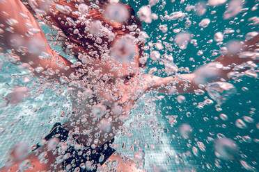 Red-haired kid diving in water raising air bubbles against a background of transparent water - ADSF07008