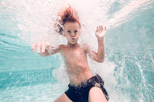 Rothaariges Kind, das im Wasser taucht und Luftblasen aufsteigen lässt, vor einem Hintergrund aus transparentem Wasser - ADSF07010