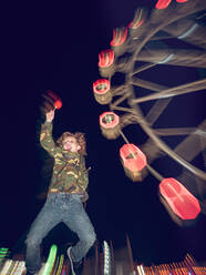 Fröhlicher kleiner Junge mit Apfel springt auf dem Hintergrund des Karussells in der Nacht. - ADSF07052