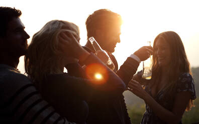 Two men and two women standing outdoors at sunset, holding beer bottles, smiling. - MINF14651
