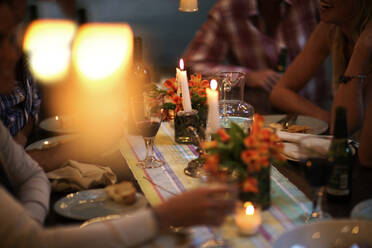 Menschen, die an einem Tisch mit Weingläsern, Tellern, Blumen und Kerzen sitzen. - MINF14656