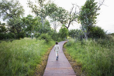 Ein sechsjähriger Junge geht auf einem Holzpfad in einem Safari-Zeltlager spazieren - MINF14680