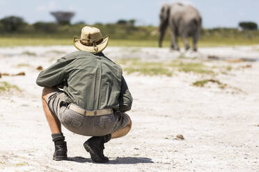 Ein Führer hockt neben einem Elefanten in der Nxai Pan, Botswana - MINF14765