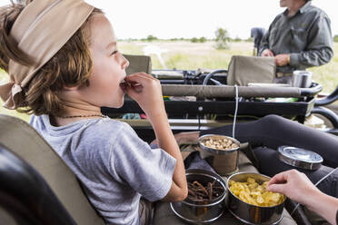 Sechsjähriger Junge isst Snacks im Safarifahrzeug, Botswana - MINF14787