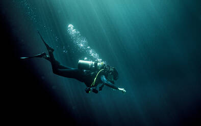 Unterwasseransicht eines Tauchers mit Neoprenanzug, Taucherbrille und Sauerstoffflasche, Luftblasen steigen auf. - MINF14817