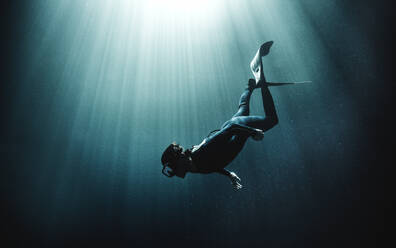 Unterwasseransicht eines Tauchers mit Neoprenanzug und Schwimmflossen, Sonnenlicht dringt von oben ein. - MINF14820
