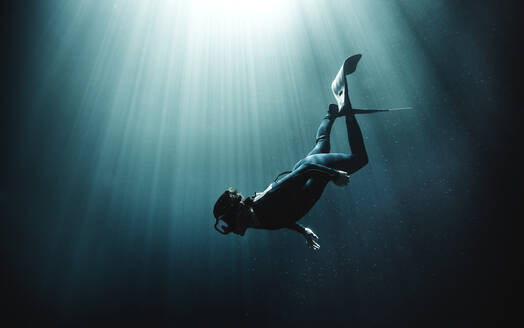 Unterwasseransicht eines Tauchers mit Neoprenanzug und Schwimmflossen, Sonnenlicht dringt von oben ein. - MINF14820