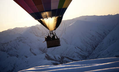 Menschen in einem Heißluftballon mitten in der Luft über einem schneebedeckten Berg. - MINF14823