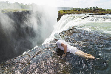 Man in the water at the Devils Pool on the edge of Victoria Falls, looking over the waterfall edge. - MINF14881