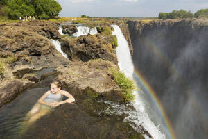 Junges Teenager-Mädchen im Wasser am Devils Pool, auf der Klippe über den Victoriafällen, Sambia, Blick von oben. - MINF14882