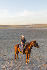 Eine Frau auf einem Pferd bei Sonnenuntergang in einer offenen Landschaft. - MINF14976