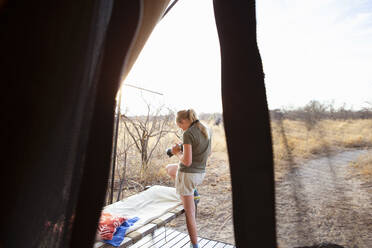 Ein zwölfjähriges Mädchen steht vor einem Zelt in einem Wildschutzgebiet und benutzt ihre Kamera. - MINF14978