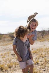 5 Jahre alter Junge mit Erdmännchen auf dem Kopf, Kalahari-Wüste, Makgadikgadi-Salzpfannen, Botswana - MINF14990
