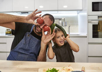 Fröhlicher Vater und Tochter spielen mit Tomaten und Zucchinis in der Küche - VEGF02586