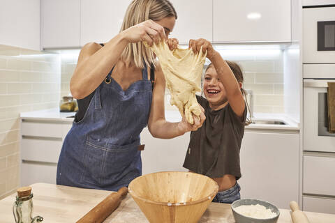 Mutter mit fröhlicher Tochter knetet Pizzateig in der Küche zu Hause, lizenzfreies Stockfoto
