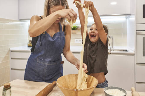 Mutter mit verspielter Tochter knetet Pizzateig in der Küche zu Hause - VEGF02590
